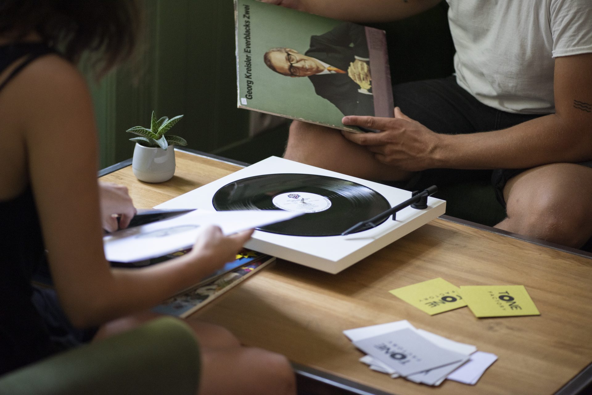 TONE turntable in use on a table by two persons sittingon the couch